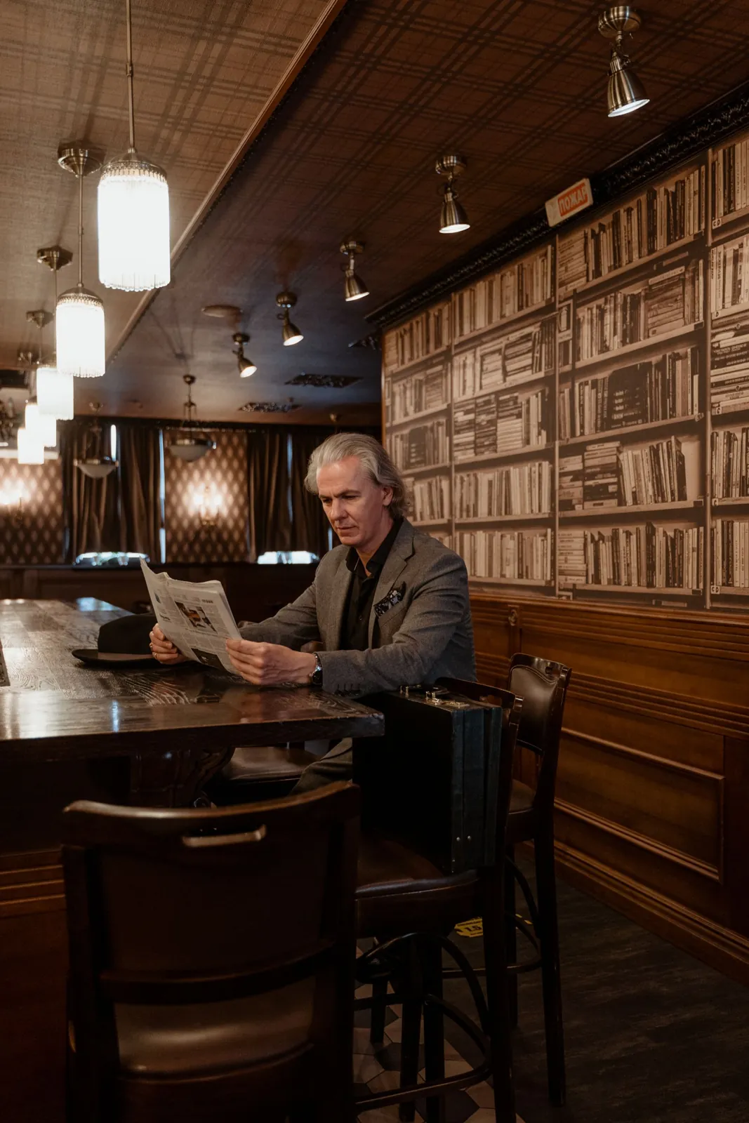 Businessman in a gray suit reading a newspaper in a library bar