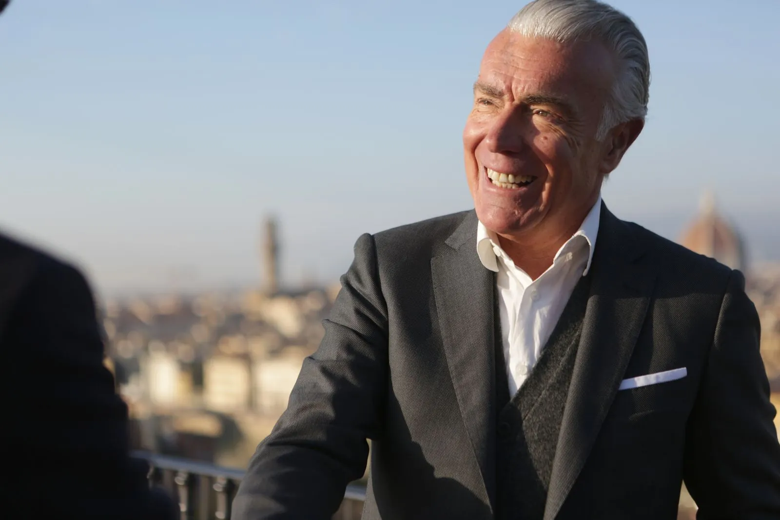 Smiling senior businessman in a dark suit with a city behind him