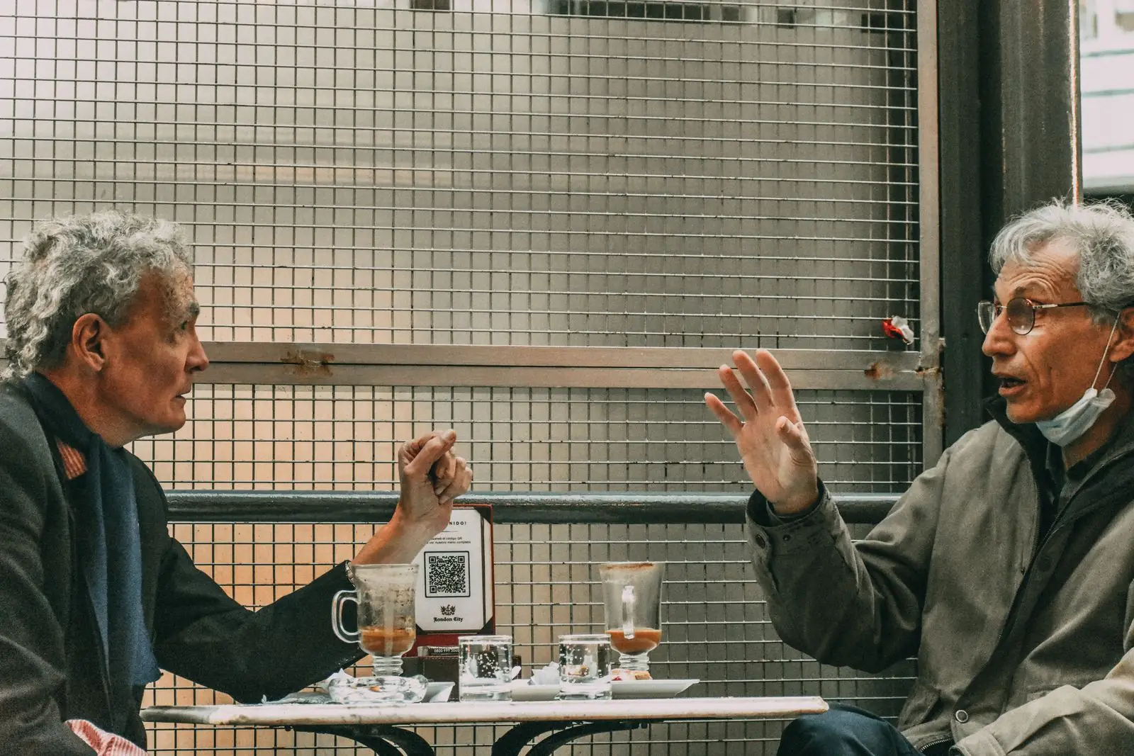 Two older men in conversation at a cafe table