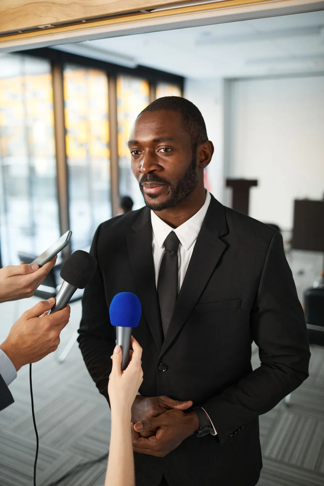 Businessman in a suit answering questions from journalists with microphones