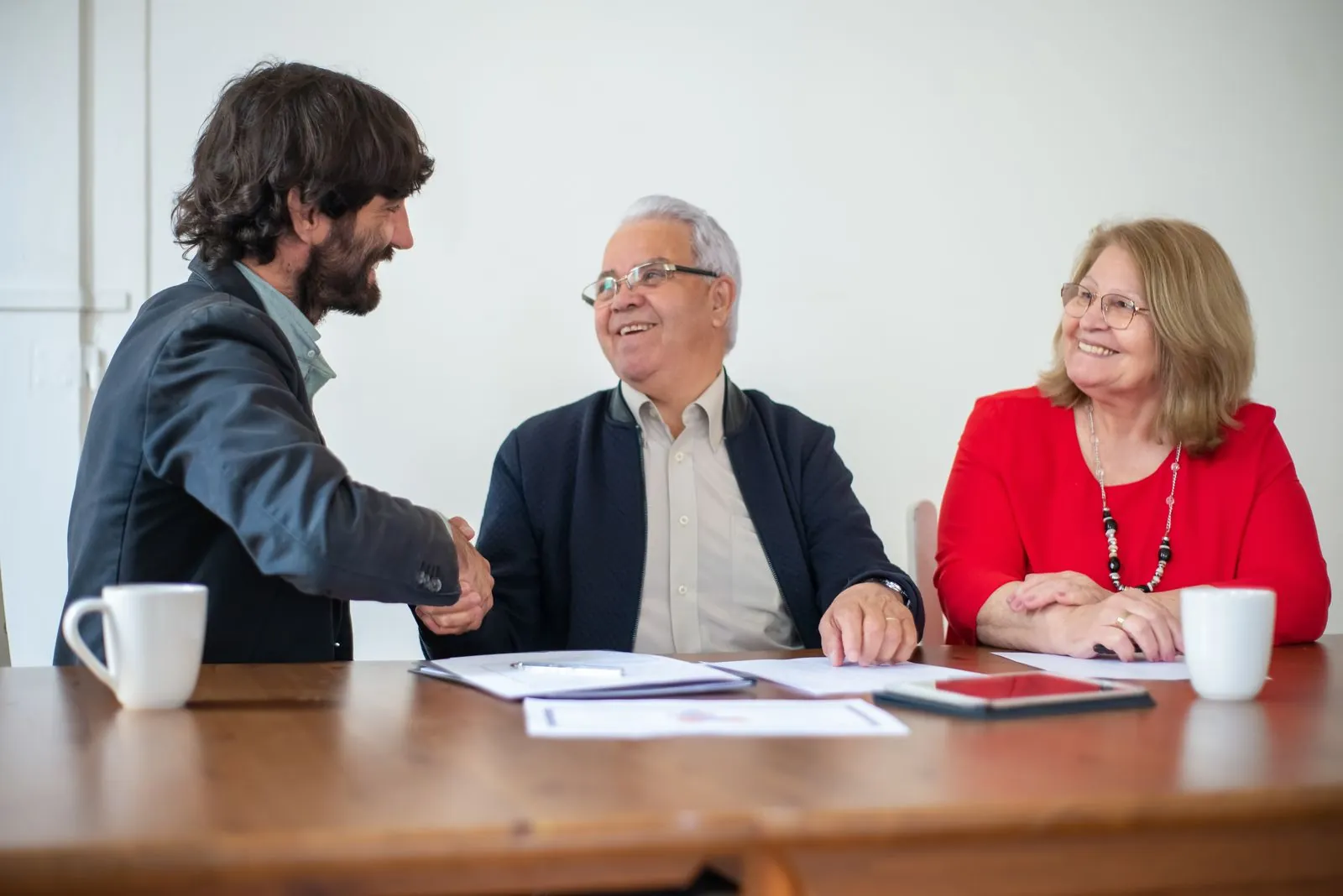 Older business owners shaking hands across a meeting table